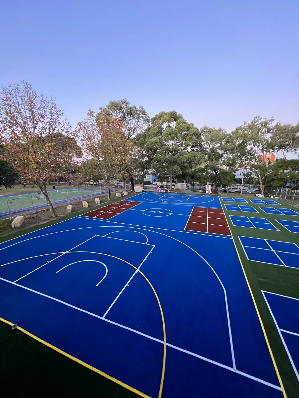 Blue acrylic multi-sport court at a school at dusk — JL Turf Group